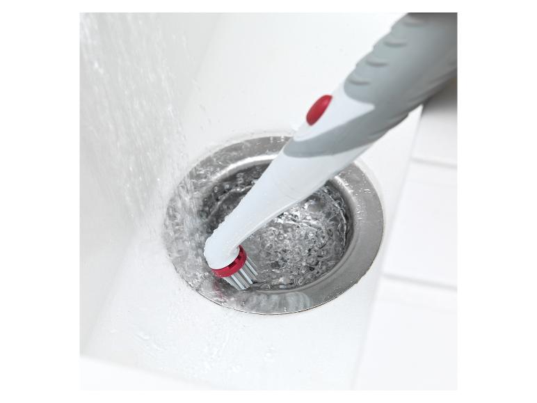 Une brosse avec un bouton rouge nettoie un évier.