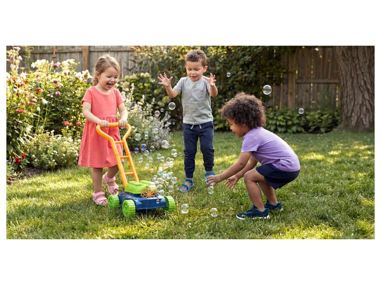 Trois enfants heureux jouent avec une tondeuse à bulles dans un jardin ensoleillé.