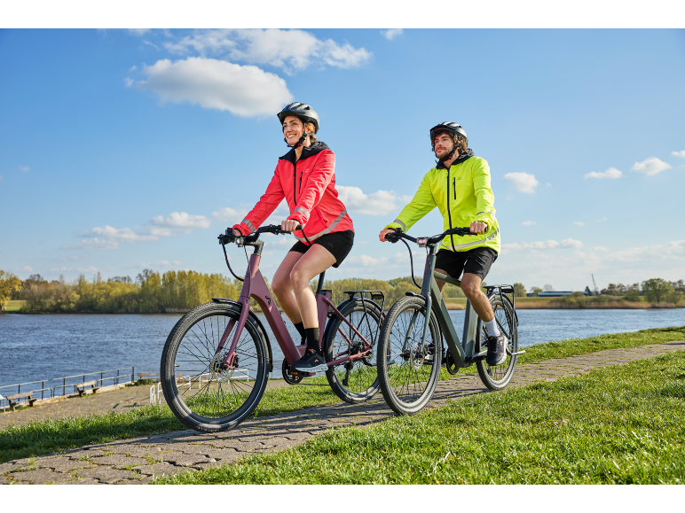 Une femme et un homme faisant du vélo électrique sur un chemin au bord de l'eau.