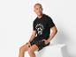 Un homme portant un t-shirt noir avec le logo 'Power Pacific' et un short à carreaux.