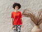 Une femme porte un t-shirt orange et un pantalon à motif tropical.
