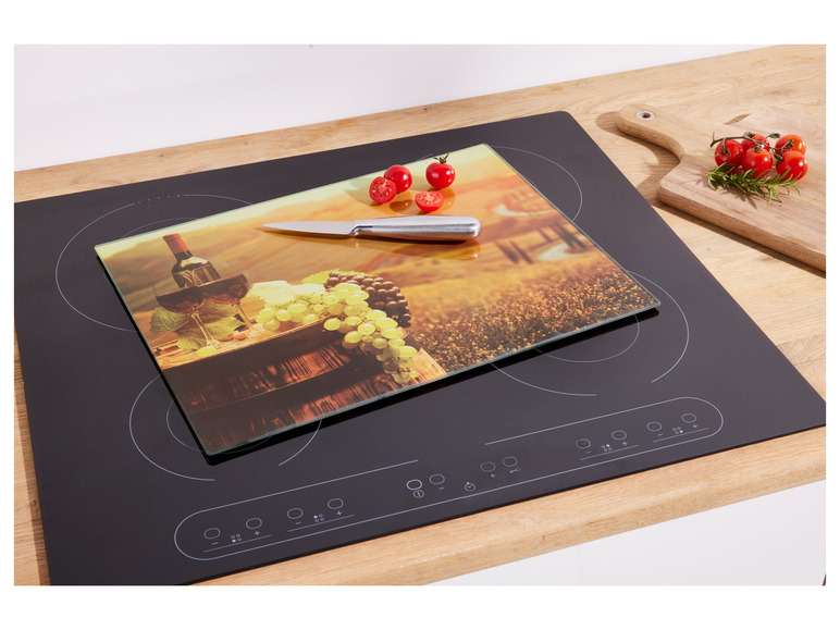 Une planche à découper en verre avec une image de vin et de raisin, sur une plaque de cuisson à induction noire.