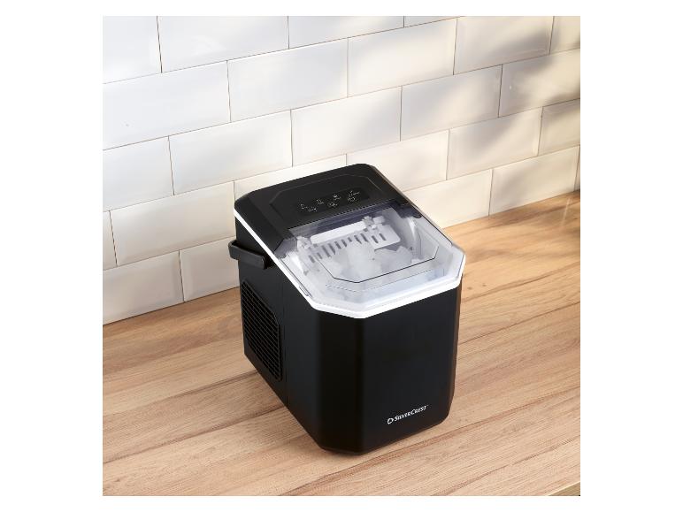 Machine à glaçons noire avec couvercle transparent, pleine de glaçons, sur un comptoir en bois.