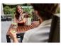 Femme souriante assise à une table en bois sur la terrasse avec boissons et fruits.