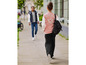 Une femme marche dans la rue avec une veste bomber rose et un sac à dos noir.