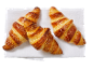 Trois croissants dorés et croustillants, saupoudrés de sucre, sur une serviette blanche.
