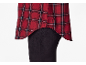 Chemise à carreaux rouge et noire avec ourlet asymétrique sur un pantalon noir.