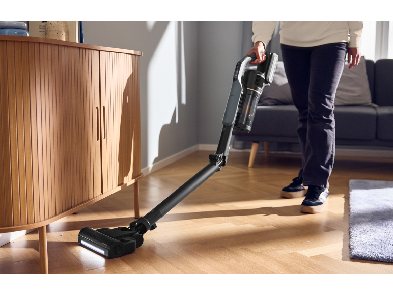 Personne passe l'aspirateur sans fil sur le sol d'un salon lumineux.