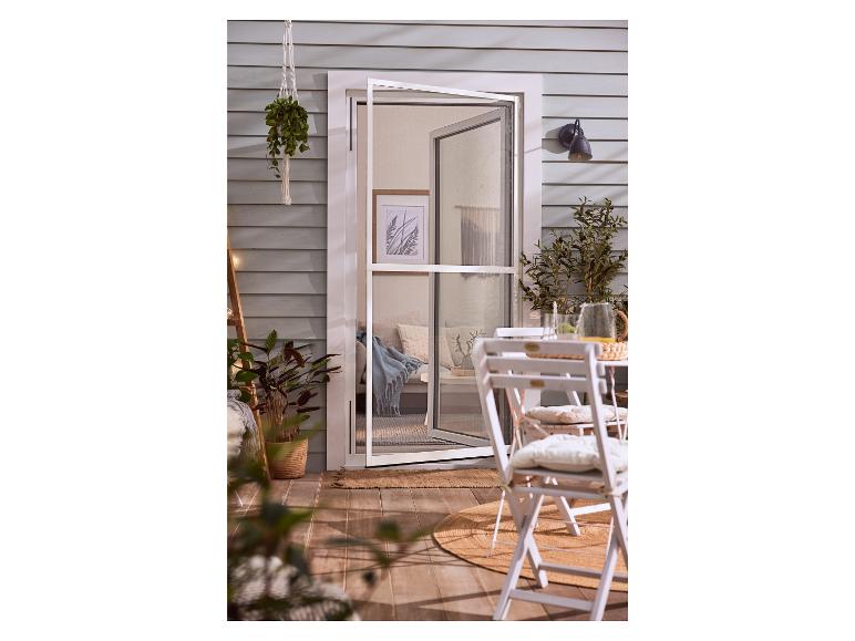 Une porte blanche avec moustiquaire, deux chaises et un tapis rond sur une terrasse.