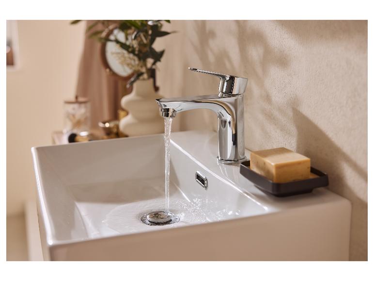 Robinet chromé avec de l'eau qui coule dans un lavabo blanc, avec du savon sur le côté.