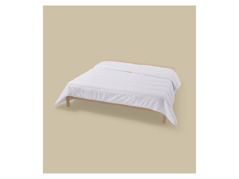 Une couette blanche sur un cadre de lit en bois clair sur fond beige.