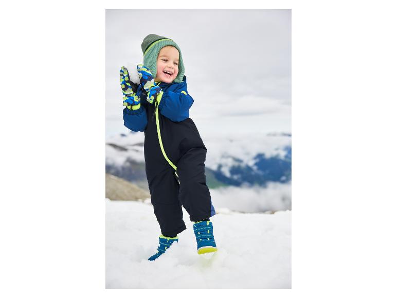 Heureux tout-petit en combinaison de neige bleue et bonnet vert jouant dans la neige.