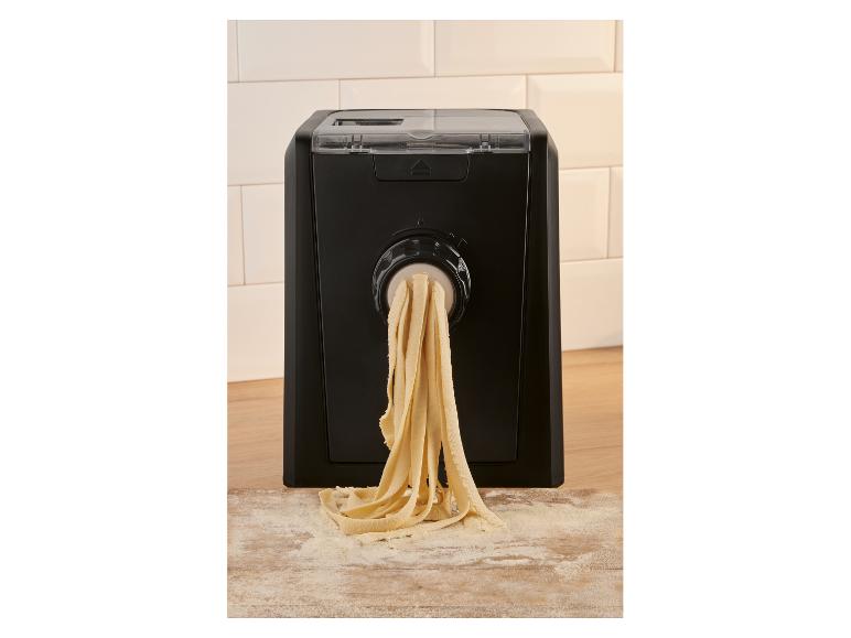 Machine à pâtes automatique extrudant des tagliatelles fraîches sur une planche en bois farinée.