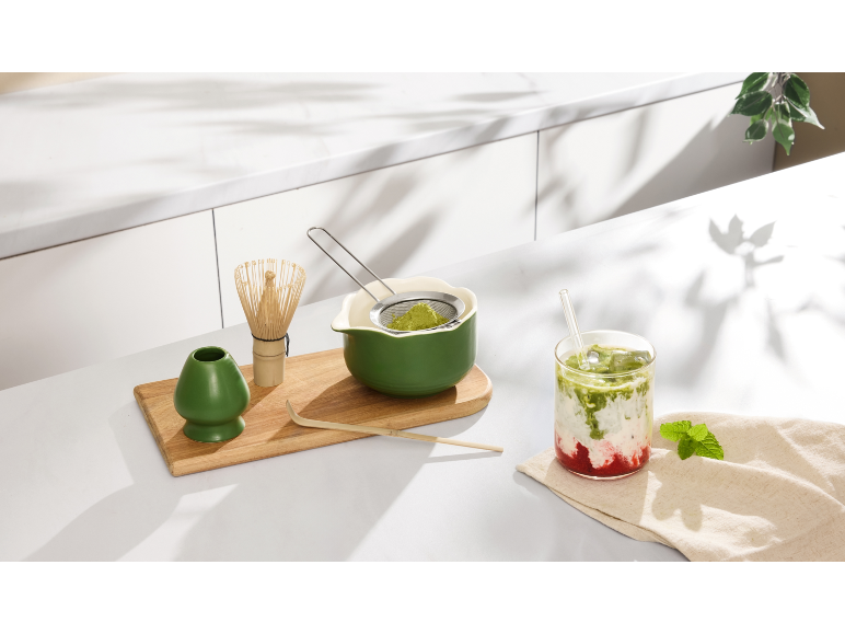 Set de préparation pour thé matcha avec un verre de matcha latte à la fraise sur un plan de travail.