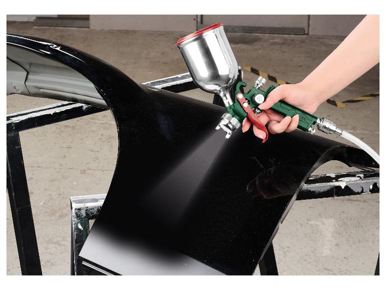 Main peignant une pièce de voiture noire avec un pistolet à peinture