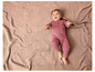 Un bébé dans une combinaison rose se trouve sur une couverture tricotée.