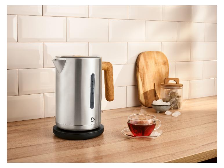 Bouilloire en acier inoxydable avec poignée en bois, une tasse de thé et accessoires sur un comptoir en bois.