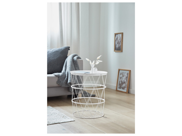 Une table basse en métal blanc avec un design tressé, à côté d'un canapé gris avec une couverture grise.