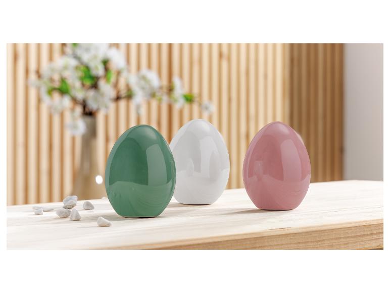 Trois pots en céramique en forme d'œuf en vert, blanc et rose sur une table en bois.