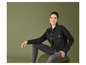 Une femme en jean noir et veste en jean pose devant un fond vert.
