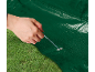 Main fixant une bâche verte à l'herbe avec un piquet de tente.