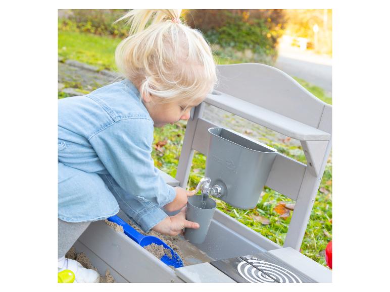 Enfant jouant avec une table à sable et à eau en bois avec robinet et seau.