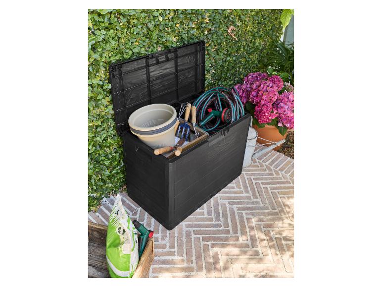 Coffre de rangement de jardin noir rempli d'outils de jardinage, d'un tuyau et d'un seau, sur une terrasse.