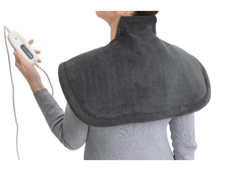Femme portant un coussin chauffant gris pour le cou et les épaules, tenant la télécommande.