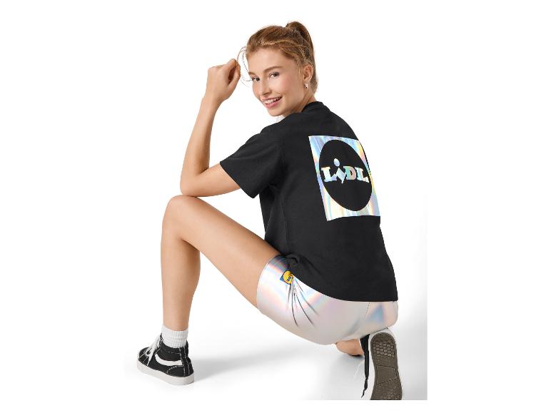 Femme en t-shirt noir avec imprimé holographique et short argenté, accroupie.