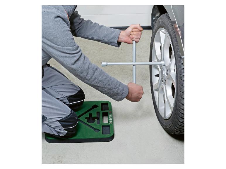 Personne agenouillée sur un tapis de travail, utilisant une clé en croix pour changer un pneu de voiture.