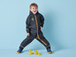 Un enfant dans une combinaison de pluie bleu foncé avec des accents jaunes et des canards en caoutchouc jaunes.