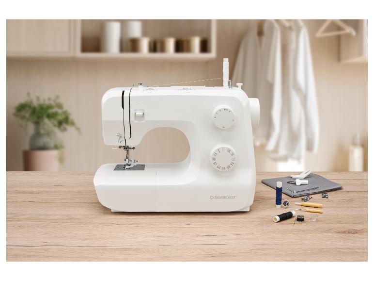 Machine à coudre blanche avec accessoires de couture sur une table en bois dans une pièce lumineuse.