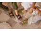 Sandales marron et vert lime sur un tapis à carreaux, portées par des personnes en pantalon décontracté.