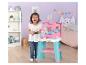 Une petite fille souriante joue avec un ensemble de cuisine rose et turquoise dans une chambre décorée sur le thème des chats.