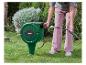 Femme connectant un tuyau d'arrosage à un enrouleur de tuyau vert dans un jardin.
