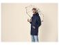 Homme en imperméable bleu marine et bonnet gris, tenant un parapluie transparent.