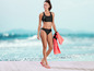 Femme en bikini noir et tongs roses sur la plage.