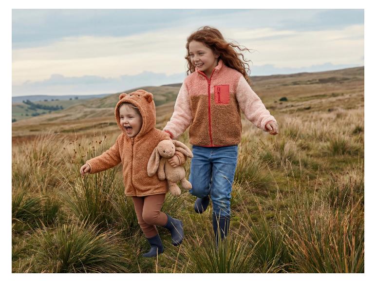 Deux enfants heureux en vestes polaires et bottes en caoutchouc courant dans un champ.