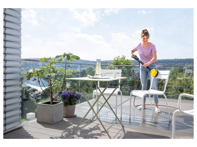 Femme nettoyant des meubles de balcon avec un nettoyeur haute pression sur un balcon avec vue.