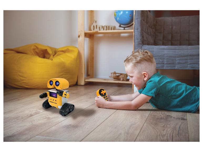 Garçon jouant avec un robot télécommandé jaune sur le sol.