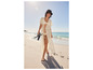 Une femme marche sur la plage en robe de plage blanche et bikini.