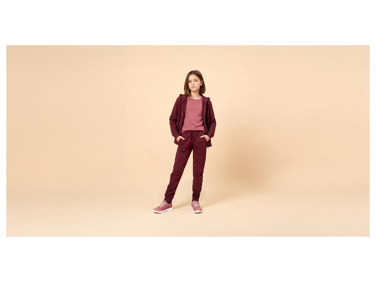 Fille en survêtement bordeaux et t-shirt rose, posant les mains dans les poches.