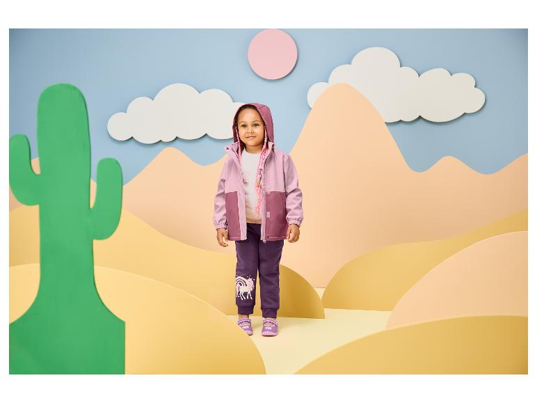 Fille en veste rose et violette et pantalon de survêtement licorne violet dans un décor désertique.