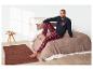 Homme en pyjama à carreaux rouges assis sur un lit.