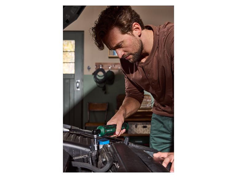 Un homme utilise une visseuse à cliquet sans fil Parkside pour réparer un moteur de voiture.