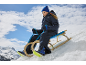 Fille en combinaison de neige et bonnet bleu, assise sur une luge en bois dans la neige.