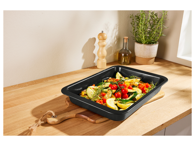 Plat à four noir contenant des légumes rôtis sur un comptoir en bois.