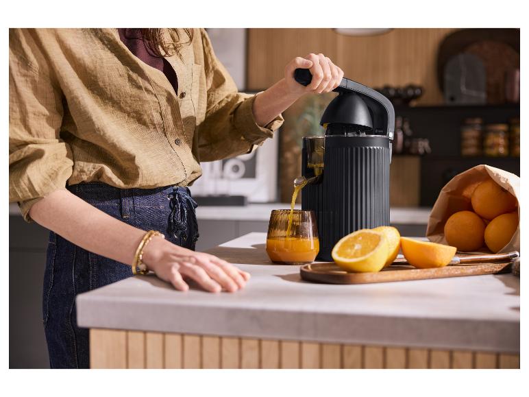 Femme pressant des oranges avec un presse-agrumes électrique noir, jus dans un verre.