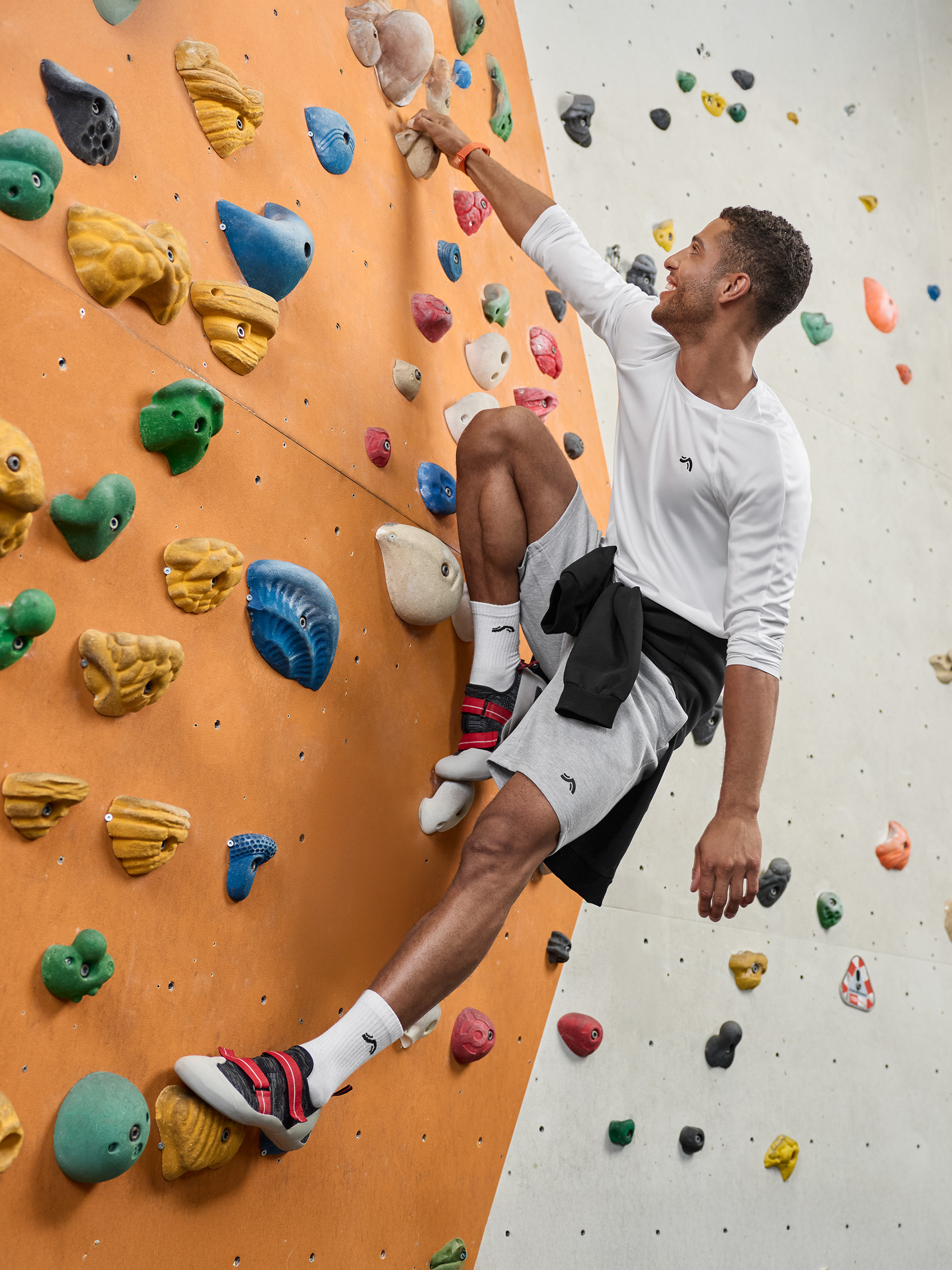 Homme en tenue de sport escaladant un mur d'escalade avec des prises colorées.