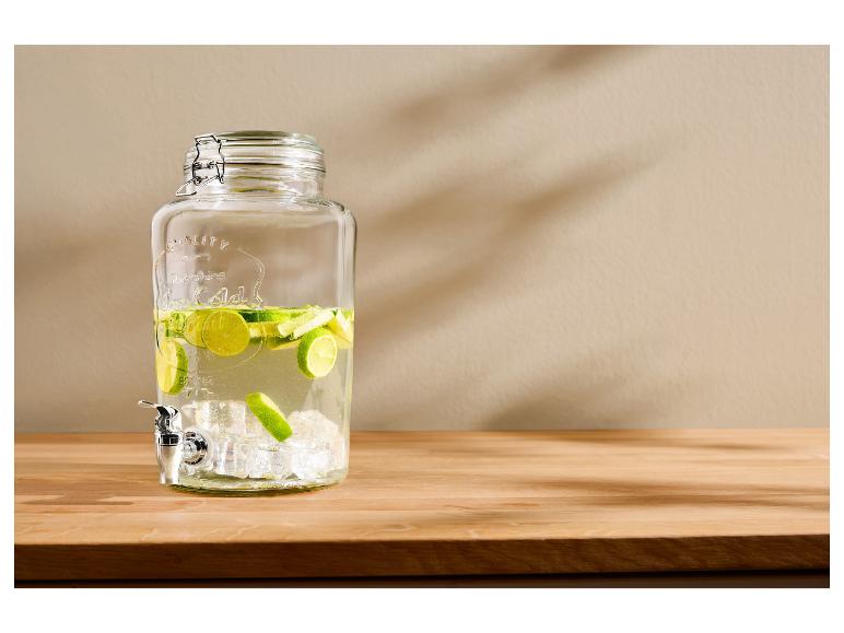 Distributeur de boissons en verre avec robinet, rempli d'eau, de tranches de citron vert et de glaçons.